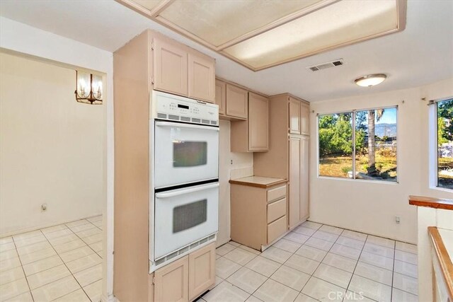 kitchen featuring light brown cabinetry, white double oven, light tile patterned floors, and pendant lighting