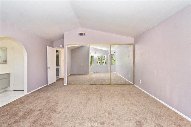 unfurnished bedroom with connected bathroom, light carpet, a closet, and lofted ceiling