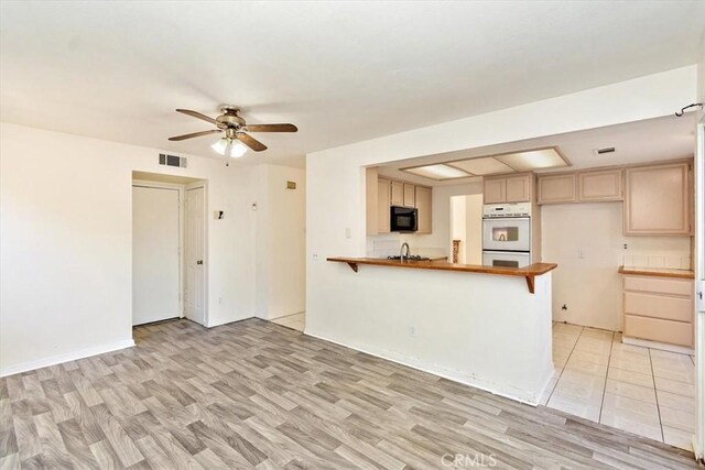 kitchen with kitchen peninsula, light wood-type flooring, double oven, and ceiling fan