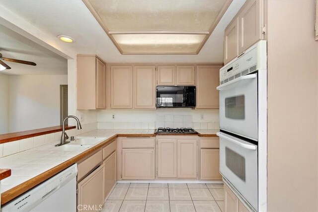 kitchen with ceiling fan, tile counters, sink, white appliances, and light tile patterned flooring