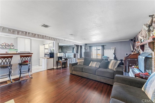 living room featuring a textured ceiling, crown molding, a stone fireplace, and dark wood-type flooring