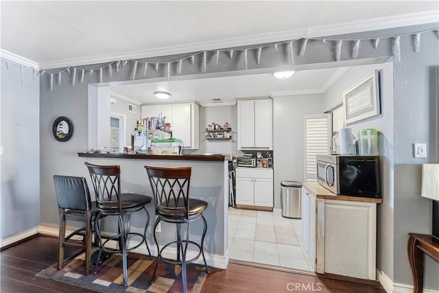 kitchen with ornamental molding, white cabinetry, kitchen peninsula, and light hardwood / wood-style flooring