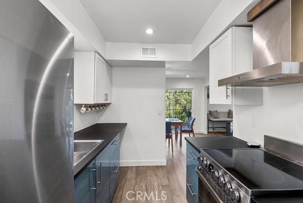 kitchen with sink, wall chimney exhaust hood, appliances with stainless steel finishes, dark hardwood / wood-style flooring, and white cabinetry