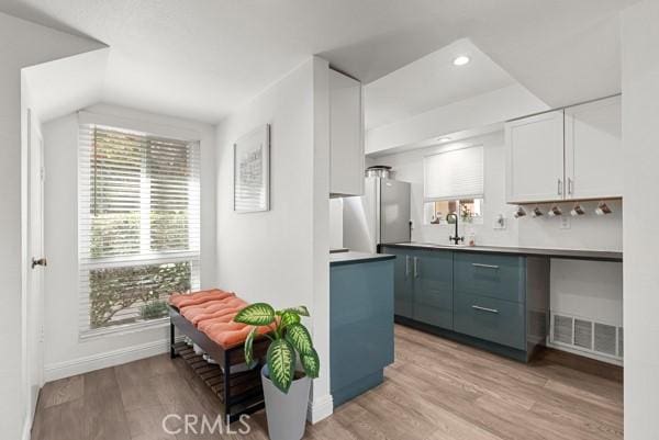 kitchen with blue cabinets, sink, white cabinets, light hardwood / wood-style floors, and stainless steel refrigerator