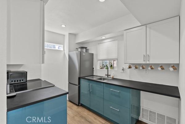 kitchen with sink, blue cabinetry, light hardwood / wood-style flooring, white cabinets, and stainless steel refrigerator