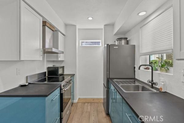 kitchen featuring sink, light hardwood / wood-style flooring, wall chimney exhaust hood, appliances with stainless steel finishes, and white cabinetry