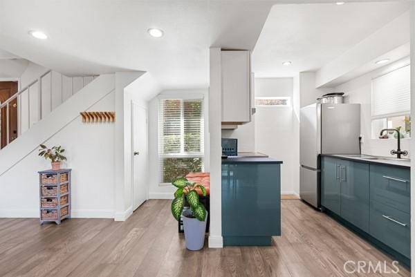 kitchen with stainless steel refrigerator, white cabinetry, light hardwood / wood-style flooring, and sink