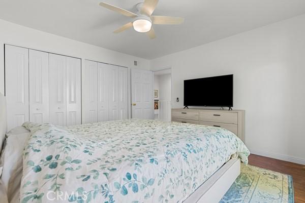 bedroom with two closets, ceiling fan, and dark wood-type flooring