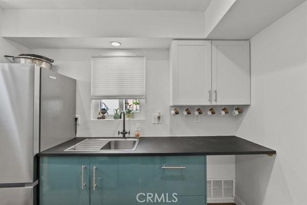 kitchen featuring white cabinets, stainless steel fridge, and sink