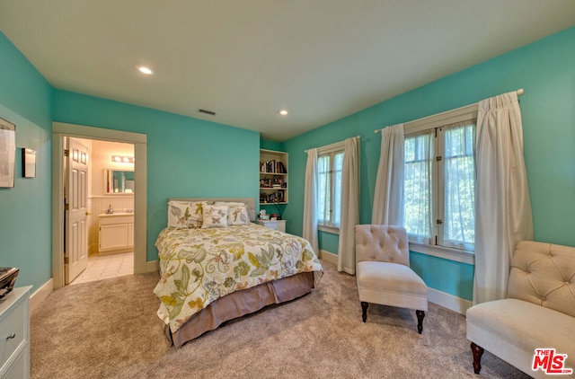 bedroom with ensuite bathroom and light colored carpet