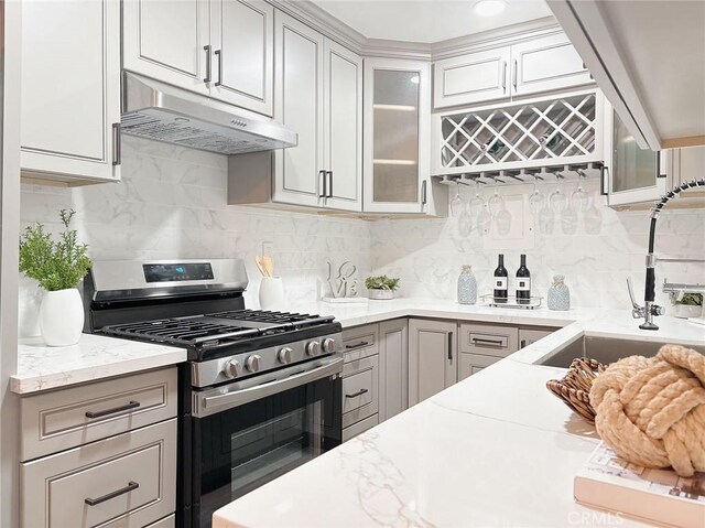 kitchen with gray cabinetry, gas stove, backsplash, light stone counters, and sink