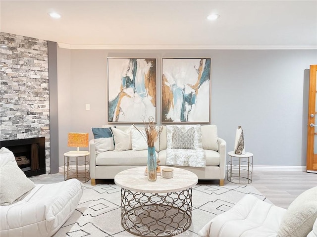 living room featuring ornamental molding, a stone fireplace, wood finished floors, and baseboards