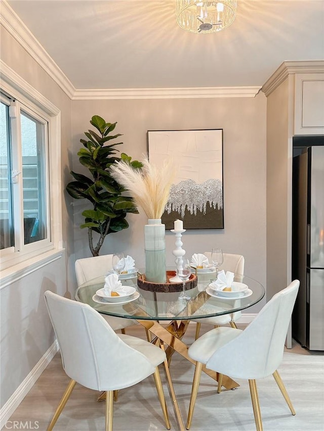 dining room with a notable chandelier, ornamental molding, light wood-style flooring, and baseboards