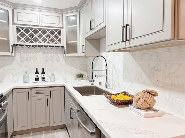 kitchen with stainless steel appliances, a sink, gray cabinets, light stone countertops, and glass insert cabinets