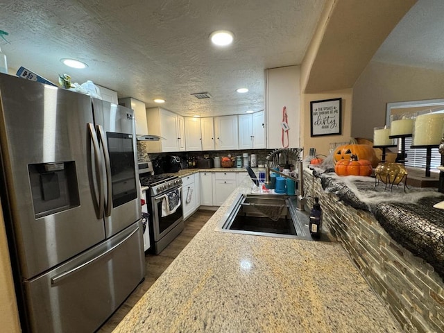 kitchen featuring wall chimney exhaust hood, decorative backsplash, light stone countertops, appliances with stainless steel finishes, and white cabinetry