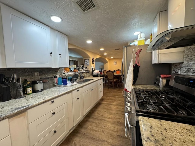 kitchen with island exhaust hood, light stone countertops, light hardwood / wood-style flooring, white cabinets, and stainless steel range with gas cooktop