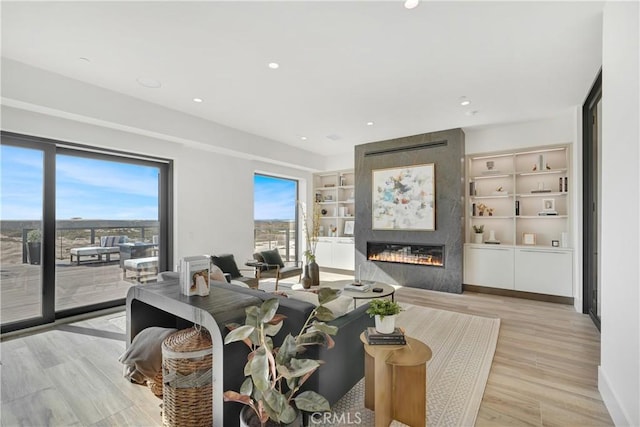 living room featuring light hardwood / wood-style flooring, a large fireplace, built in features, and plenty of natural light