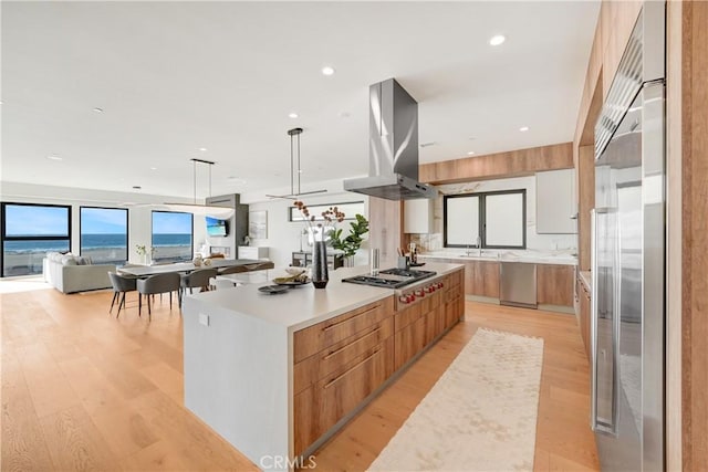 kitchen with island range hood, a large island, stainless steel appliances, hanging light fixtures, and a water view