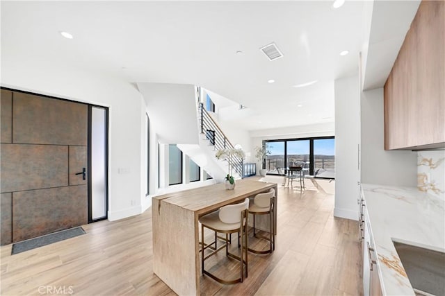 kitchen featuring light brown cabinetry, light hardwood / wood-style flooring, light stone counters, and a breakfast bar