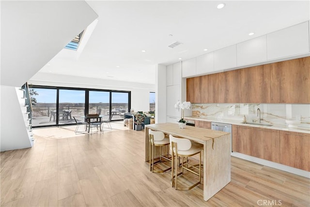 kitchen with light hardwood / wood-style floors, sink, a kitchen breakfast bar, and white cabinets