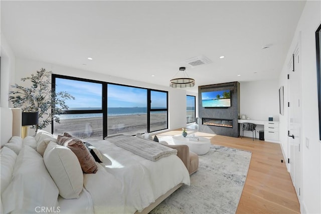 bedroom featuring a large fireplace, light hardwood / wood-style floors, a water view, and a beach view