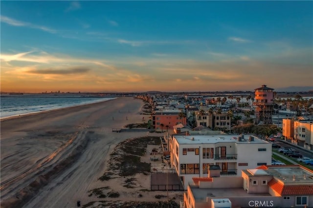 aerial view at dusk featuring a water view and a view of the beach