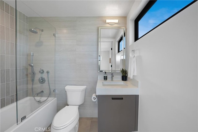 full bathroom featuring tile patterned flooring, vanity, bath / shower combo with glass door, toilet, and tile walls