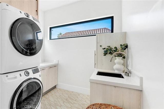 washroom with stacked washer / drying machine, light tile patterned floors, sink, and cabinets