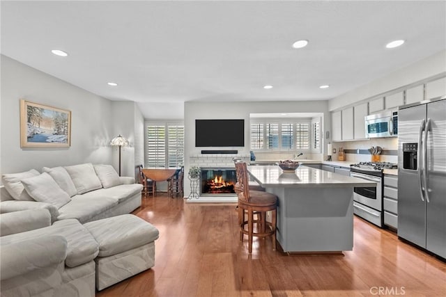 kitchen with appliances with stainless steel finishes, light hardwood / wood-style flooring, a center island, white cabinetry, and a breakfast bar area