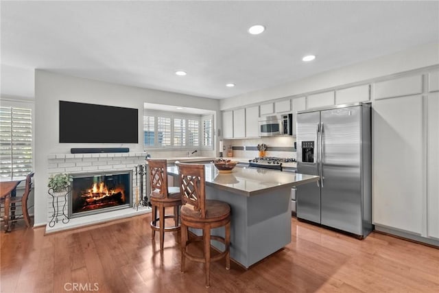 kitchen with white cabinetry, a center island, a breakfast bar area, appliances with stainless steel finishes, and light wood-type flooring