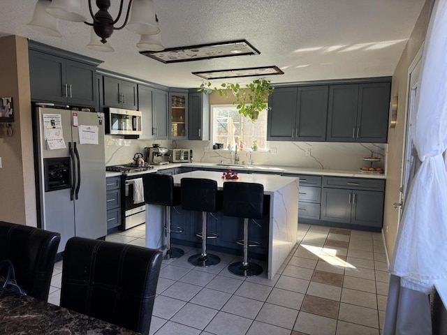 kitchen featuring light tile patterned flooring, a center island, a kitchen breakfast bar, gray cabinets, and stainless steel appliances