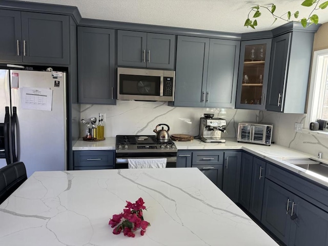 kitchen featuring sink, gray cabinets, appliances with stainless steel finishes, light stone counters, and tasteful backsplash