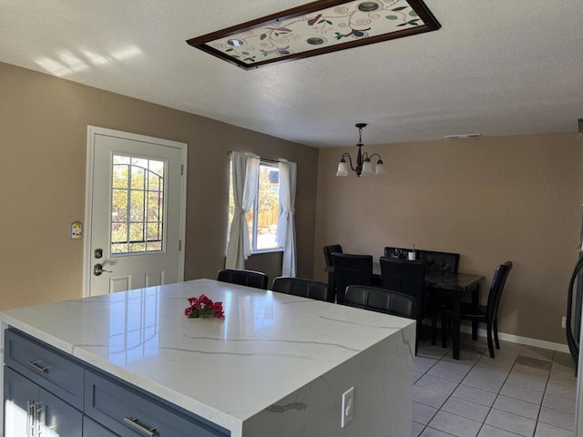 kitchen featuring hanging light fixtures, a notable chandelier, a textured ceiling, a kitchen island, and light tile patterned flooring