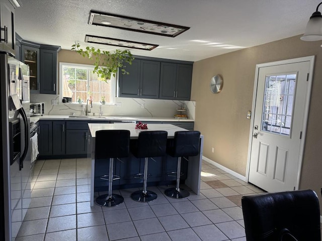 kitchen with sink, a breakfast bar area, a kitchen island, light tile patterned flooring, and stainless steel fridge with ice dispenser