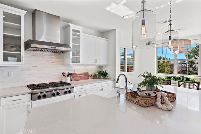 kitchen with sink, wall chimney range hood, pendant lighting, stainless steel gas stovetop, and white cabinets