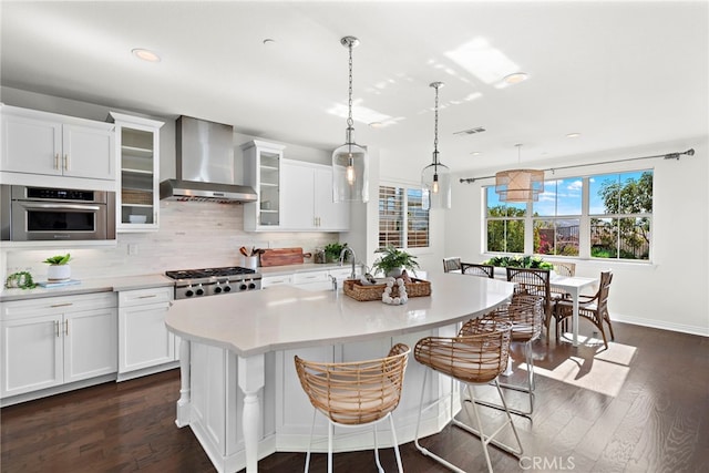 kitchen featuring an island with sink, dark wood-type flooring, wall chimney range hood, and appliances with stainless steel finishes