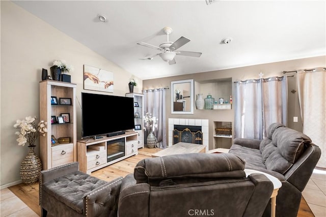 living room with a tile fireplace, light hardwood / wood-style flooring, vaulted ceiling, and ceiling fan