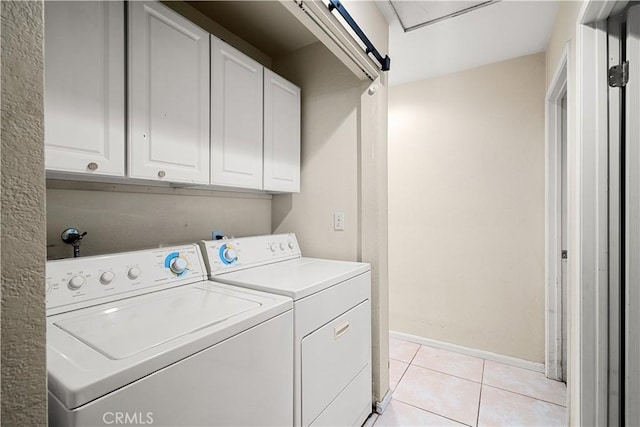 clothes washing area featuring washing machine and clothes dryer, a barn door, light tile patterned floors, and cabinets