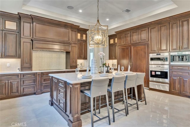 kitchen with a center island with sink, pendant lighting, a raised ceiling, and stainless steel double oven