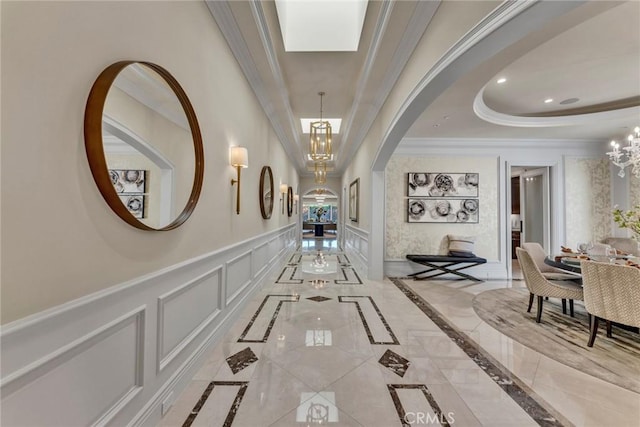 corridor with ornamental molding, a tray ceiling, a skylight, and a notable chandelier