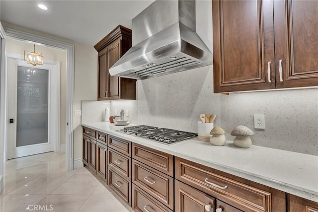 kitchen featuring wall chimney exhaust hood, an inviting chandelier, stainless steel gas cooktop, decorative backsplash, and light tile patterned floors