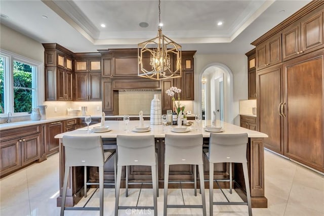 kitchen featuring pendant lighting, a center island with sink, a raised ceiling, a notable chandelier, and a breakfast bar area