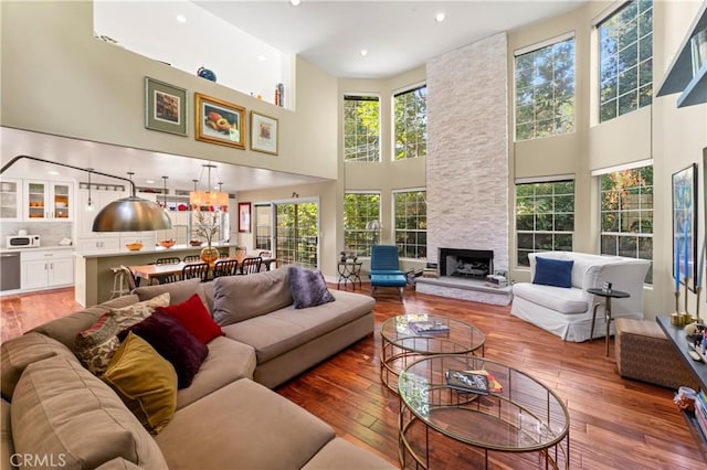 living room with wood-type flooring, a towering ceiling, a wealth of natural light, and a fireplace