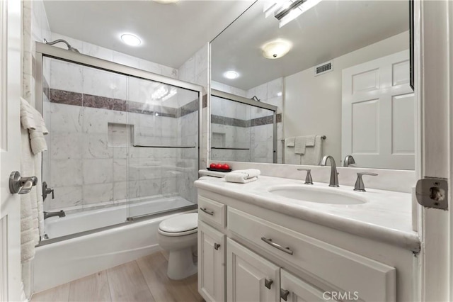 full bathroom with vanity, hardwood / wood-style flooring, shower / bath combination with glass door, and toilet