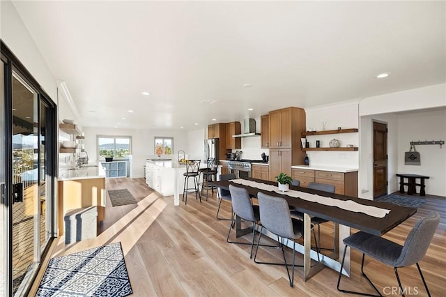 kitchen with stainless steel range, light wood-type flooring, kitchen peninsula, and wall chimney exhaust hood