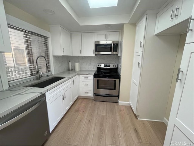 kitchen with light stone countertops, sink, appliances with stainless steel finishes, white cabinets, and light wood-type flooring