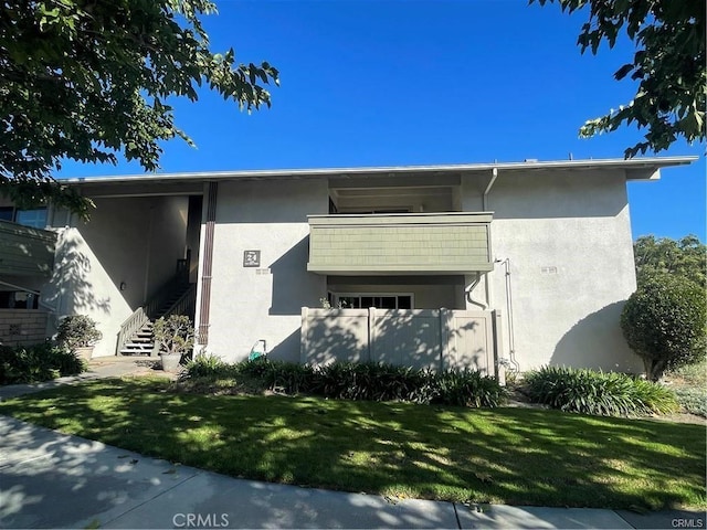 exterior space with a front yard, a balcony, stairs, and stucco siding