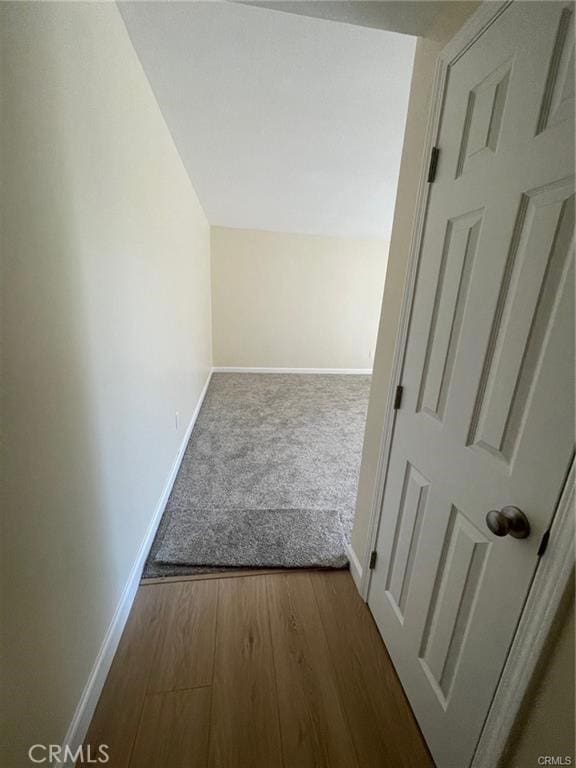 corridor featuring lofted ceiling, baseboards, and wood finished floors