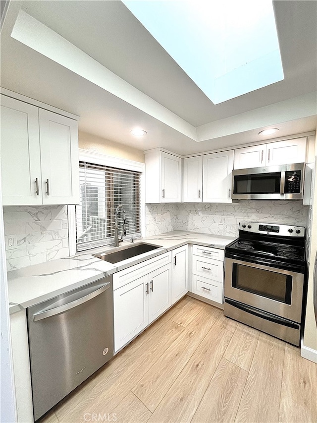 kitchen with light wood finished floors, stainless steel appliances, tasteful backsplash, white cabinetry, and a sink