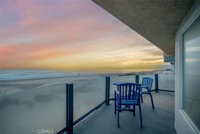 balcony at dusk with a water view and a beach view